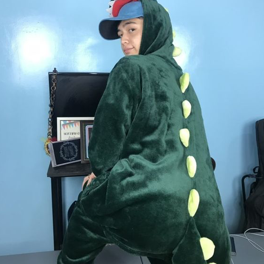 A photo of Noel wearing a green dinosaur onesie and posing showing his backside