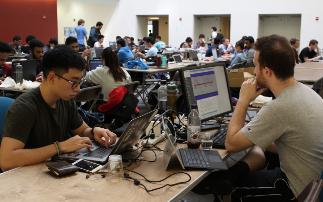 Students working on laptops at a hackathon.